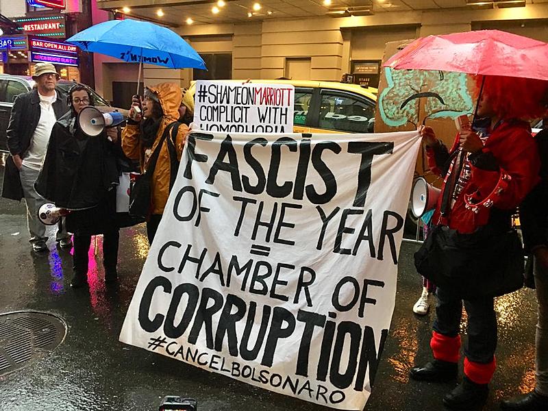 Manifestante com faixa com os dizeres "Fascista do Ano" e "Câmera da Corrupção" em ato em Nova York