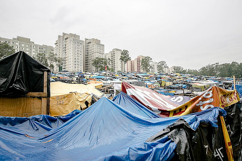 Juntos, os integrantes enfrentam o sol embaixo das lonas pretas ou a chuva forte que entra nos barracos e molha os poucos os pertences.