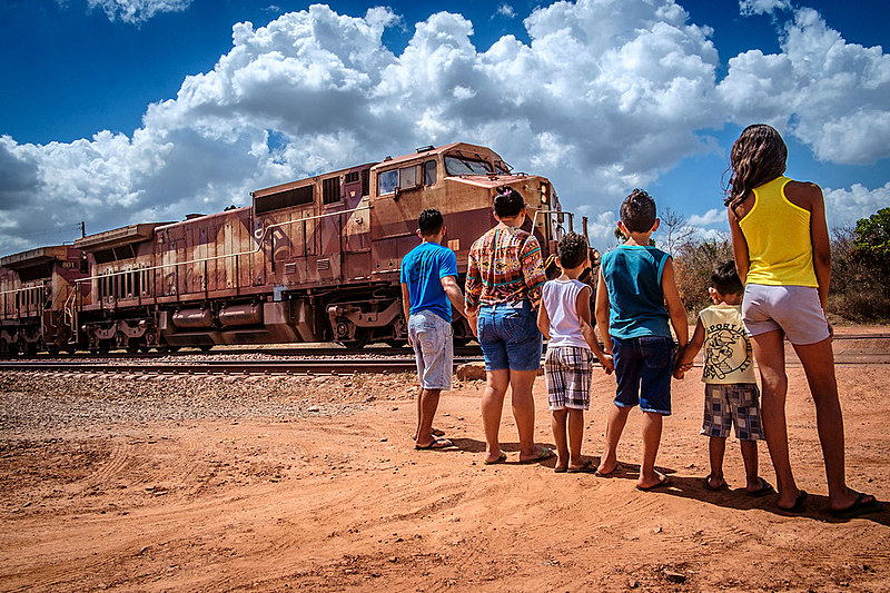 Família a espera que o trem, carregado de minério, passe para atravesar