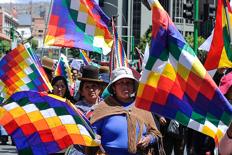 Manifestantes marcham na capital de Bolívia, La Paz, carregando bandeiras wiphala, símbolo dos povos originários