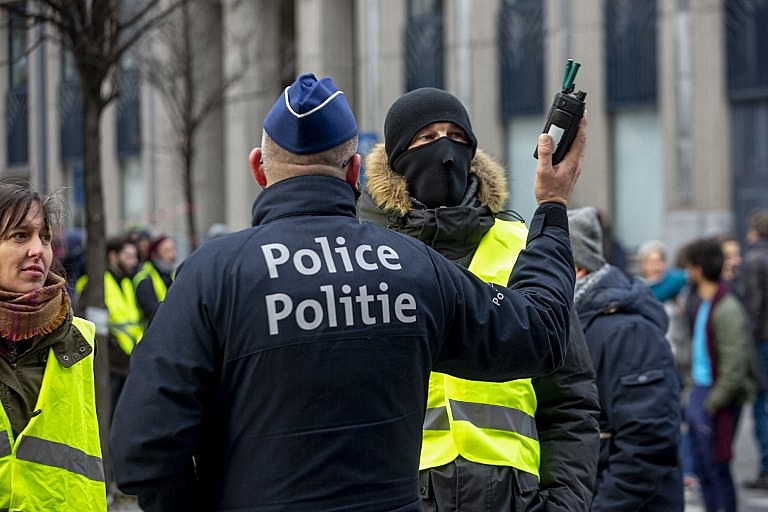 Policial belga conversa com manifestantes vestidos com coletes amarelos durante protesto no centro de Bruxelas no sábado