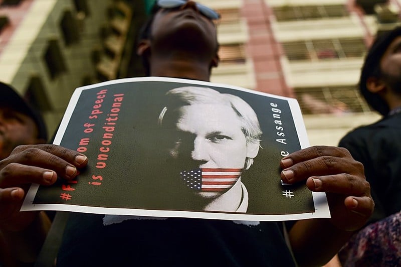 Manifestante segura foto de Assange amordaçado pela bandeira dos EUA em ato realizado em Bangladesh em abril de 2019