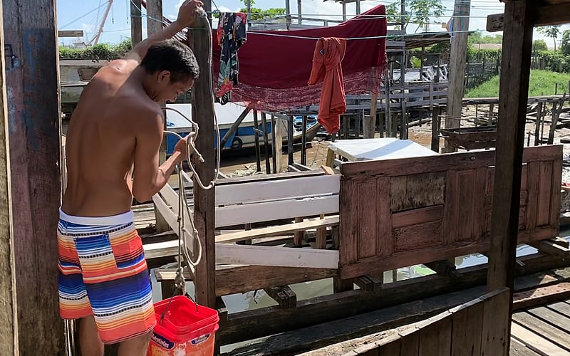 Morador da comunidade da Vila da Barca puxando água com a ajuda de um balde.