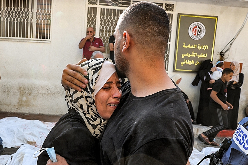 Homem conforta mulher palestina em luto à frente do necrotério de um hospital na cidade de Gaza, nesta quinta (12), após ataques de Israel em reação ao Hamas