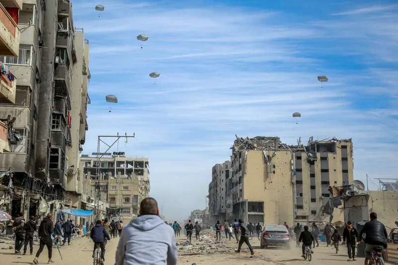 Palestinos correm ao longo de uma rua enquanto a ajuda humanitária é lançada por via aérea na cidade de Gaza