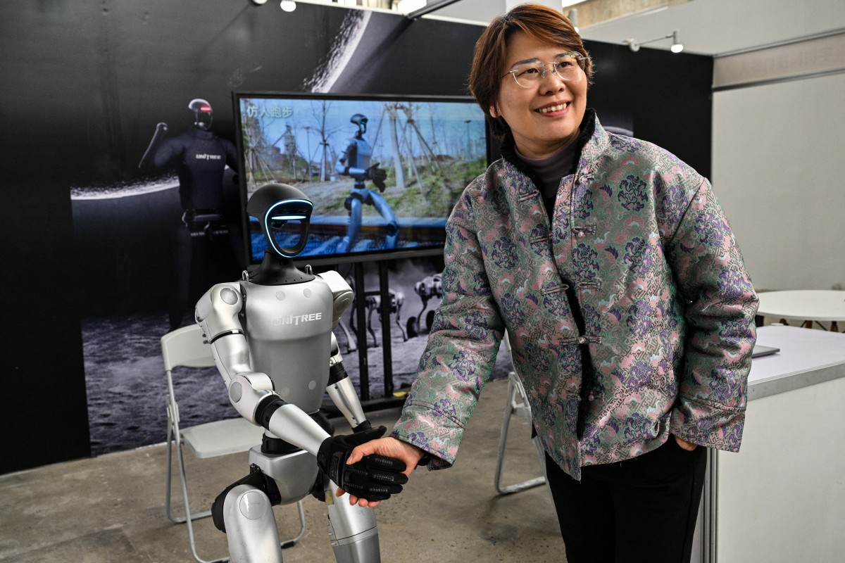 Uma mulher aperta a mão de um robô humanoide da Unitree Robotics durante a Global Developer Conference, em Xangai - em 21 de fevereiro de 2025
