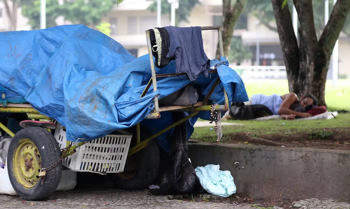 Pessoas em situação de rua dorme em praça ao lado de carrinho para coleta de materiais recicláveis