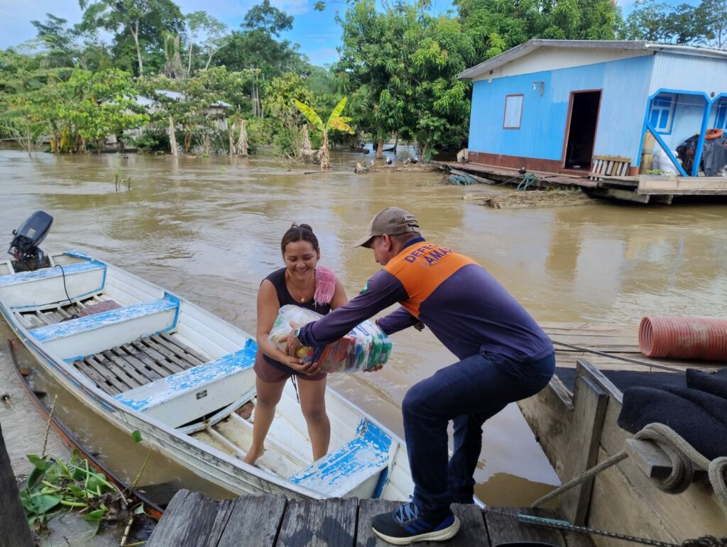 Funcionário da Defesa Civil do Amazonas entrega cesta básica para mulher em cidade atingida pelas cheias dos rios da região
