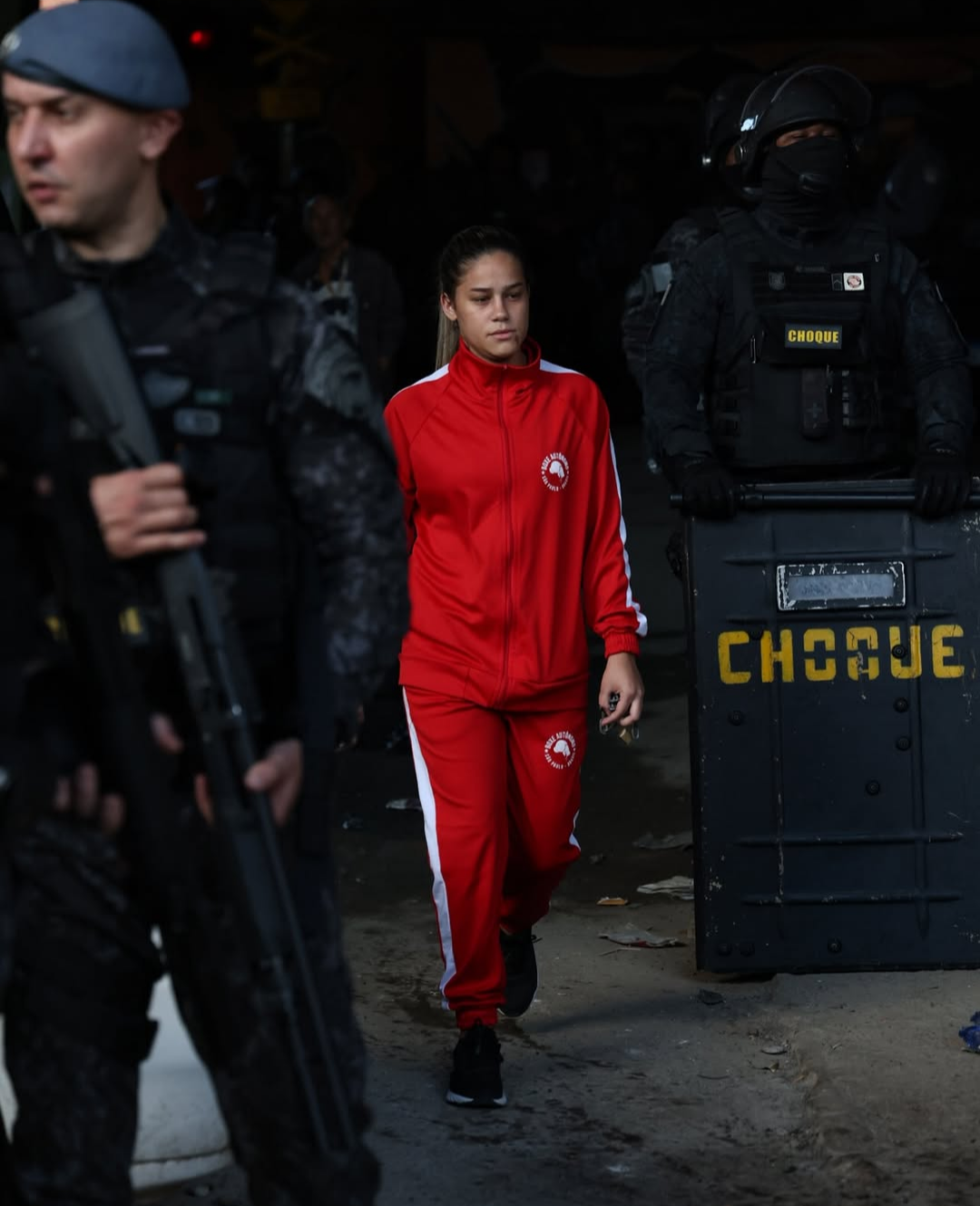 mulher com agasalho esportivo passa por policiais com escudos