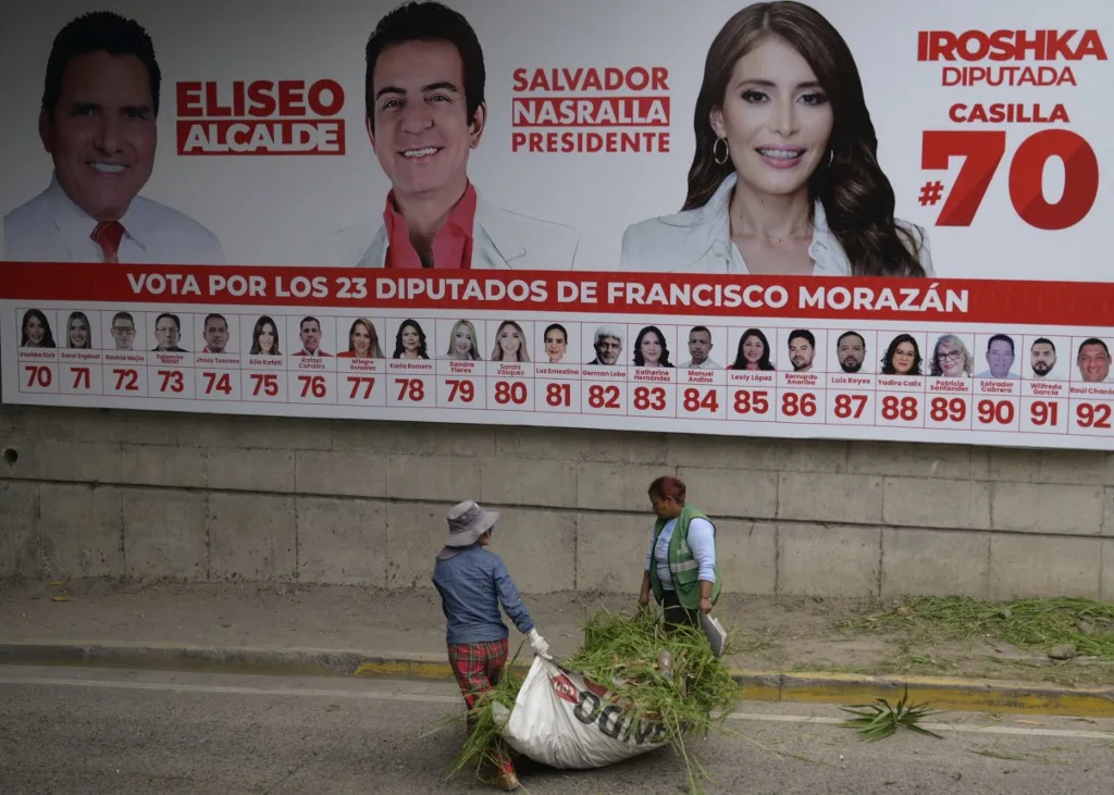 Povos indígenas caminham em frente a um outdoor do candidato presidencial Salvador Nasralla, do Partido Liberal, em Tegucigalpa, em 5 de novembro de 2025. (Foto de Orlando SIERRA / AFP)