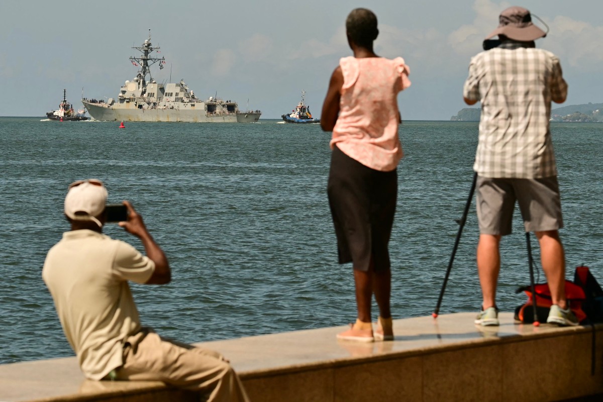 People watch and take pictures of the USS Gravely, a US Navy warship, departing the Port of Port of Spain on October 30, 2025. The US warship arrived in Trinidad and Tobago on October 26, 2025, for joint exercises near the coast of Venezuela, as Washington ratcheted up pressure on drug traffickers and Venezuelan leader Nicolas Maduro.