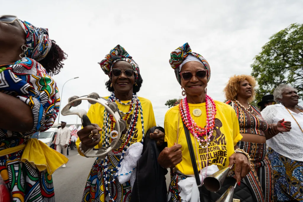 Duas mulheres negras na marcha, com blusas amarelas.