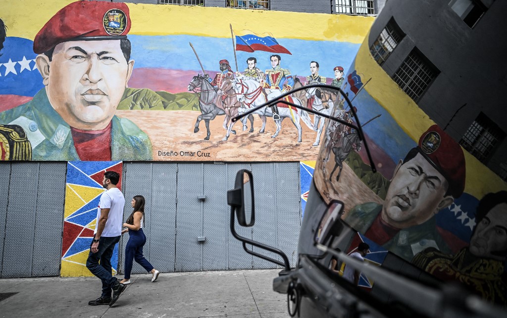 Pessoas passam por um mural que retrata o ex-presidente venezuelano Hugo Chávez ao lado de heróis da independência da Venezuela em Caracas, em 17 de dezembro de 2025.