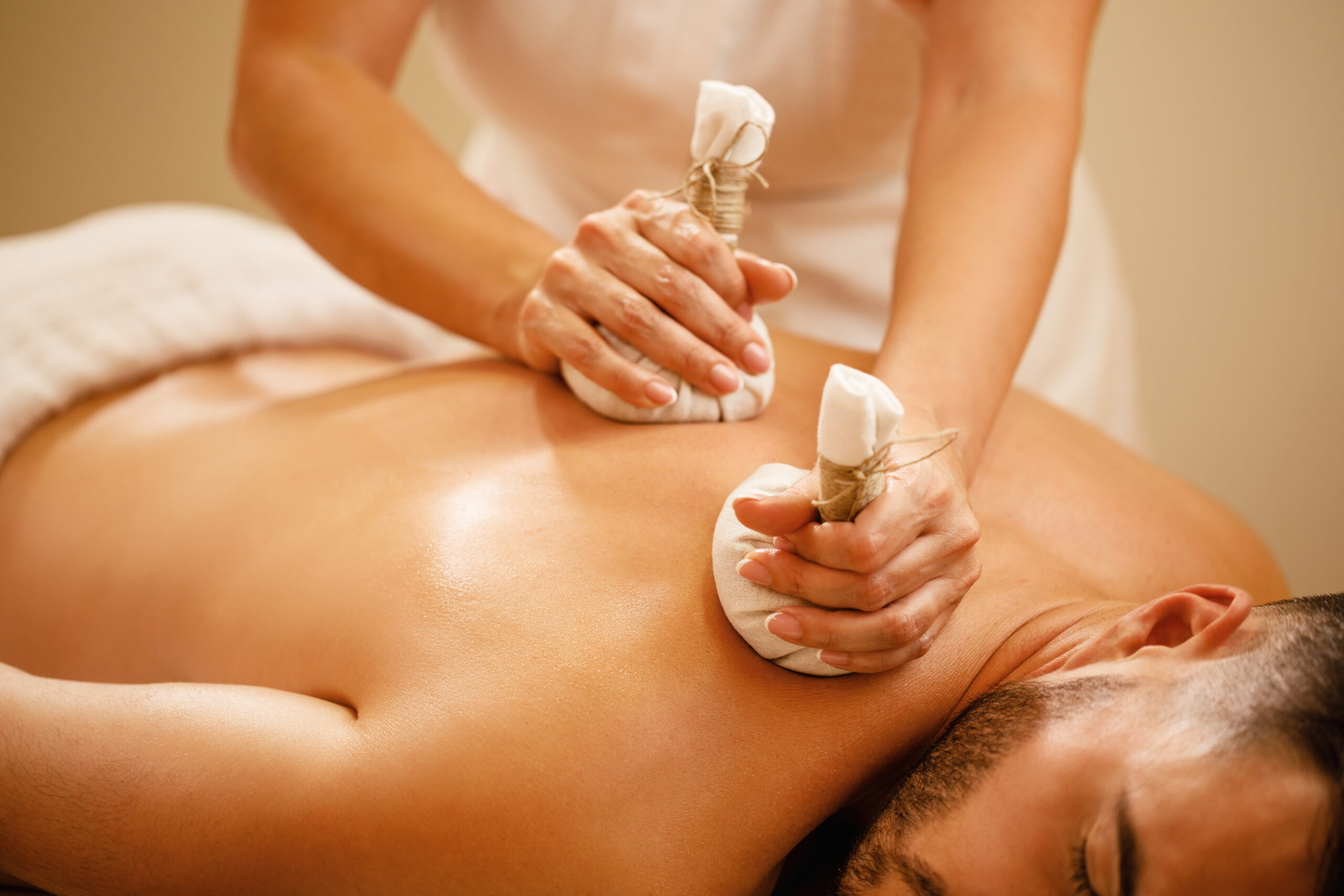 Close-up of man getting back massage with detox herbal balls at health spa.