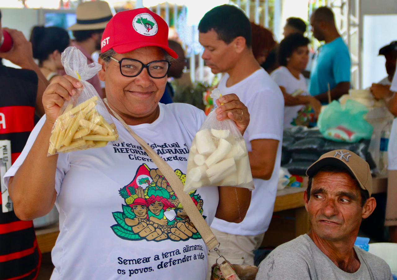 Expositora com boné do MST exibe alimentos comercializados na feira