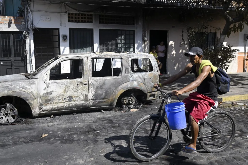 Um homem passa de bicicleta por um veículo queimado em Puerto Vallarta, no estado de Jalisco, México, em 24 de fevereiro de 2026.