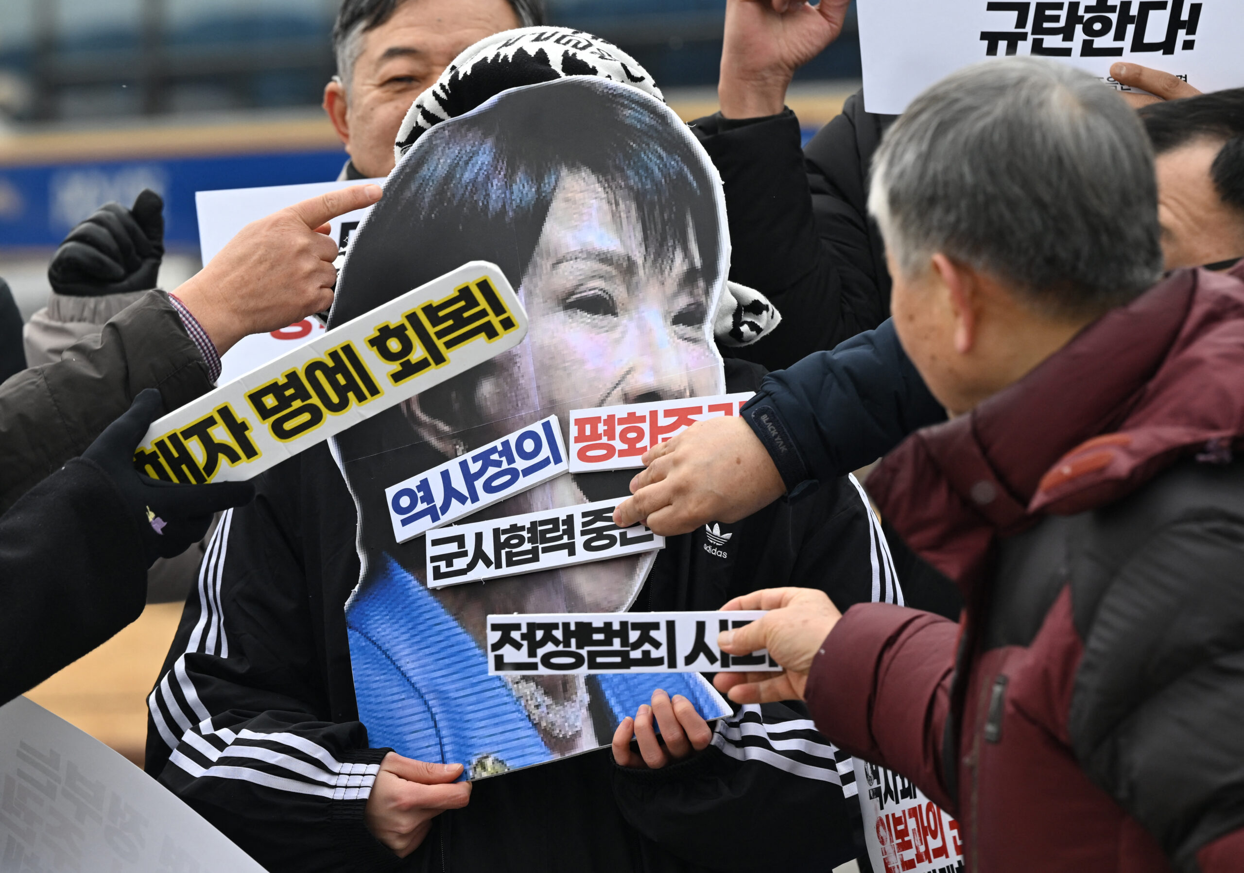 Ativistas sul-coreanos colocam frases com os dizeres "Parem a cooperação militar" e "Peça desculpas pelos crimes de guerra" em um recorte de papelão da primeira-ministra japonesa Sanae Takaichi durante um protesto , em Seul, em 12 de janeiro de 2026, antes da viagem do presidente sul-coreano Lee Jae-myung ao Japão.