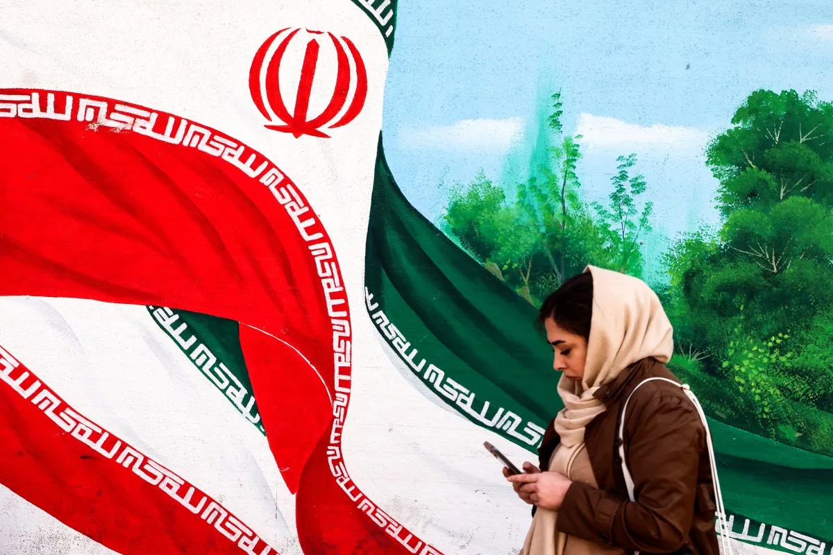 Mulher iraniana caminha ao lado de um mural com a bandeira do Irã em Teerã, em fevereiro de 2026