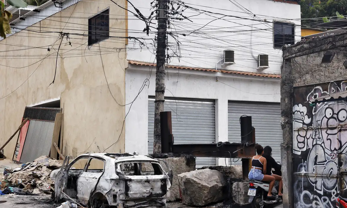 Pessoas passam em moto na praça da Vila Cruzeiro ao lado de barricadas que foram colocadas para conter avanço de policiais durante a Operação Contenção. Foto: Tânia Rêgo/Agência Brasil© Tânia Rêgo/Agência Brasil