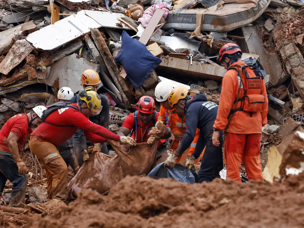 Soldados do Corpo de Bombeiros e voluntários fazem busca e resgate de pessoas em escombros de casas soterradas por lama após fortes chuvas