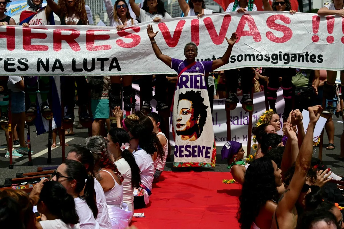 Mulher participa de ato do 8 de Março no Rio de Janeiro envolta em faixa com a imagem de Marielle Franco e a palavra “Presente”, em 8 de março de 2026. Marielle, vereadora e defensora dos direitos humanos, foi assassinada em 2018
