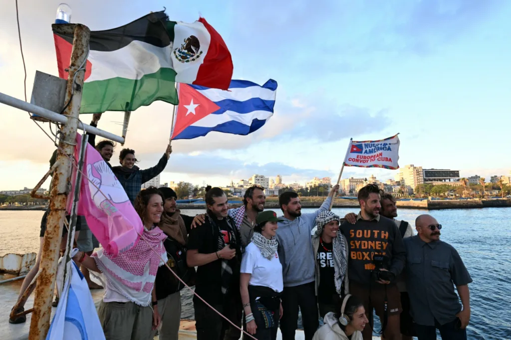 Ativistas exibem bandeiras de Cuba, México e Palestina a bordo do Maguro, rebatizado de “Granma 2.0”, na chegada ao porto de Havana com ajuda humanitária vinda do México, em 24 de março de 2026.