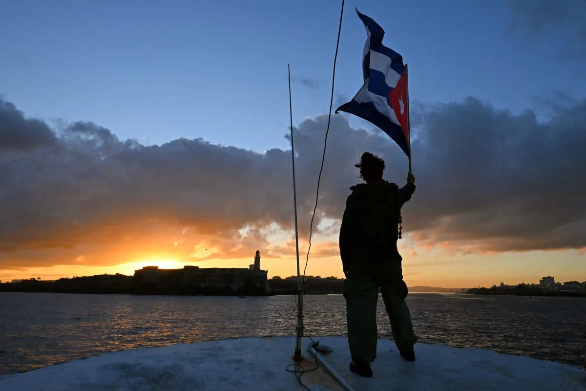 Uma ativista acena com uma bandeira cubana a bordo da embarcação Maguro -- simbolicamente renomeada "Granma 2.0" em homenagem ao iate usado pelos guerrilheiros de Fidel Castro para lançar sua revolução em 1956 -- que chega do México com ajuda humanitária como parte do comboio Nuestra América, atracando no porto de Havana em 24 de março de 2026