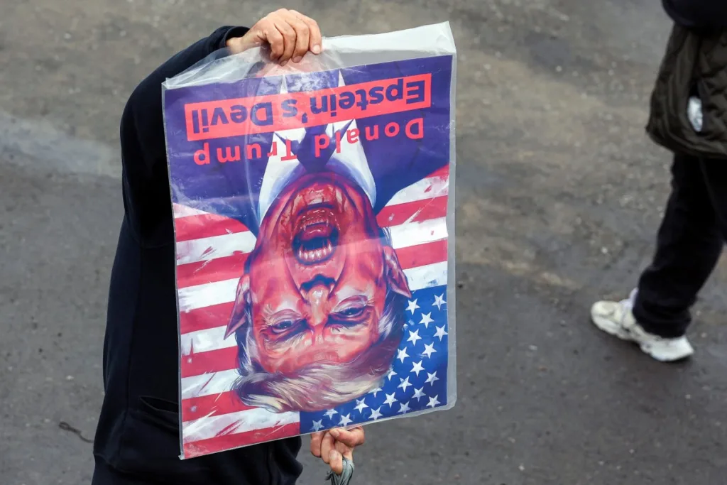 A mourner holds a cartoon denouncing the US President Donald Trump and associating him with the late convicted US sex offender Jeffrey Epstein, during the funeral ceremony for Iran's slain intelligence minister Esmail Khatib and his family after the weekly Friday Muslim noon prayers in Tehran on March 20, 2026. Israel's military said on March 18 that it would not stop its "series of eliminations" of senior Iranian officials, after announcing it had killed Khatib. His killing came soon after Israel killed Iran's powerful security chief Ali Larijani. (Photo by AFP)