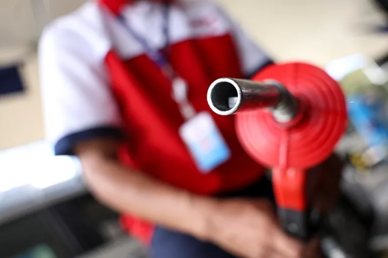 Na imagem, um frentista uniformizado, sem que apareça seu rosto, segura um bico de abastecimento com suporte vermelho