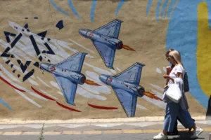 Mulheres iranianas caminham em frente a um mural anti-EUA e anti-Israel em Teerã, em 3 de junho de 2026.
