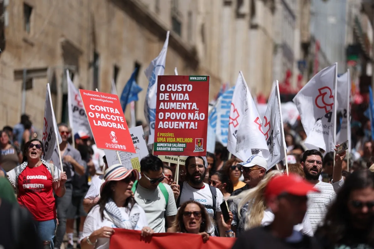 People with a poster reading The cost pot living rises and te people cant stand it and waving trade union flags as they line the streets during a demonstration in Lisbon called by the main unions due to a 24-hour general strike over proposed labour reforms. The stoppage hit transport companies as well as waste collection, hospitals and schools, according to the General Confederation of Portuguese Workers (CGTP). (Photo by PATRICIA DE MELO MOREIRA / AFP)