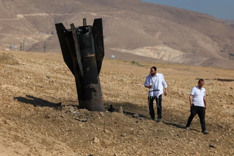 Dois homens examinam um foguete caído, parcialmente enterrado no solo, nos arredores de Jericó, Cisjordânia, em 8 de junho