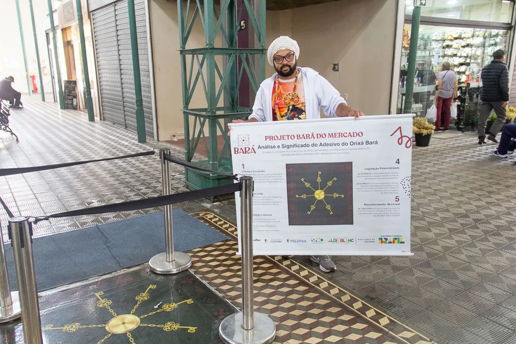 Pai Juliano com o banner do projeto Bará do Mercado ao lado do assentamento do orixá