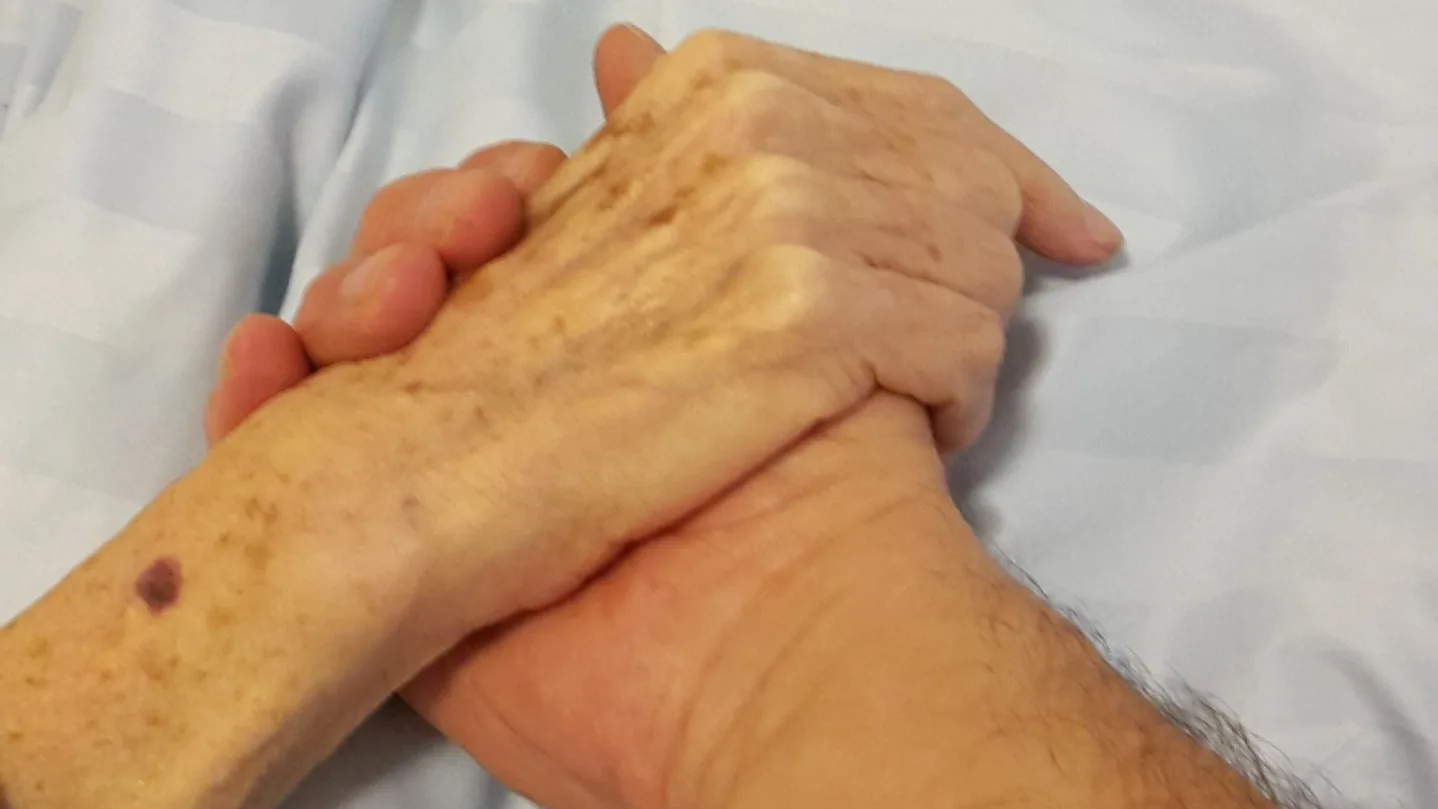 Fotografia mostra as mãos de uma pessoa idosa unidas sobre o peito