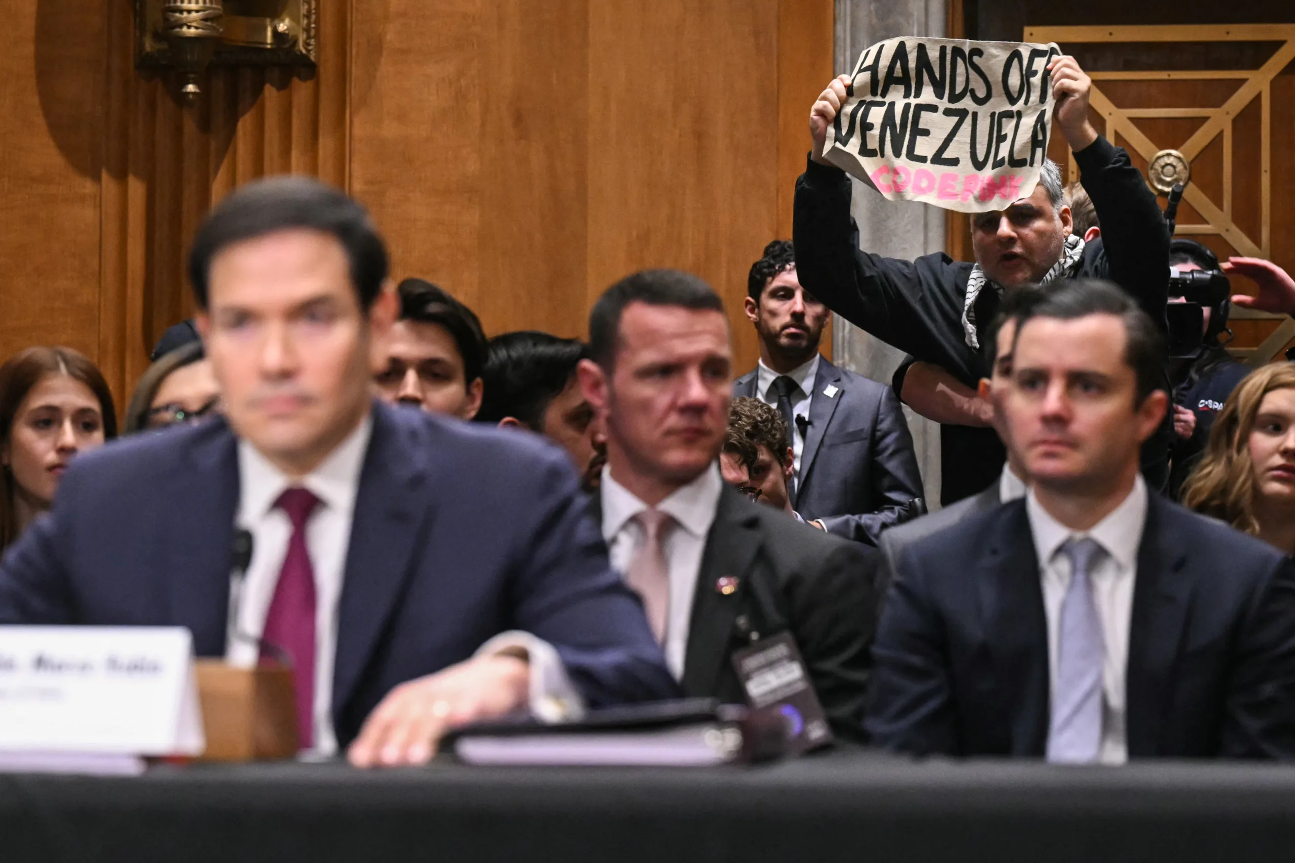 Um manifestante segura um cartaz enquanto o Secretário de Estado dos EUA, Marco Rubio, presta depoimento durante uma audiência do Comitê de Relações Exteriores do Senado, em Washington, DC, em 28 de janeiro de 2026.
