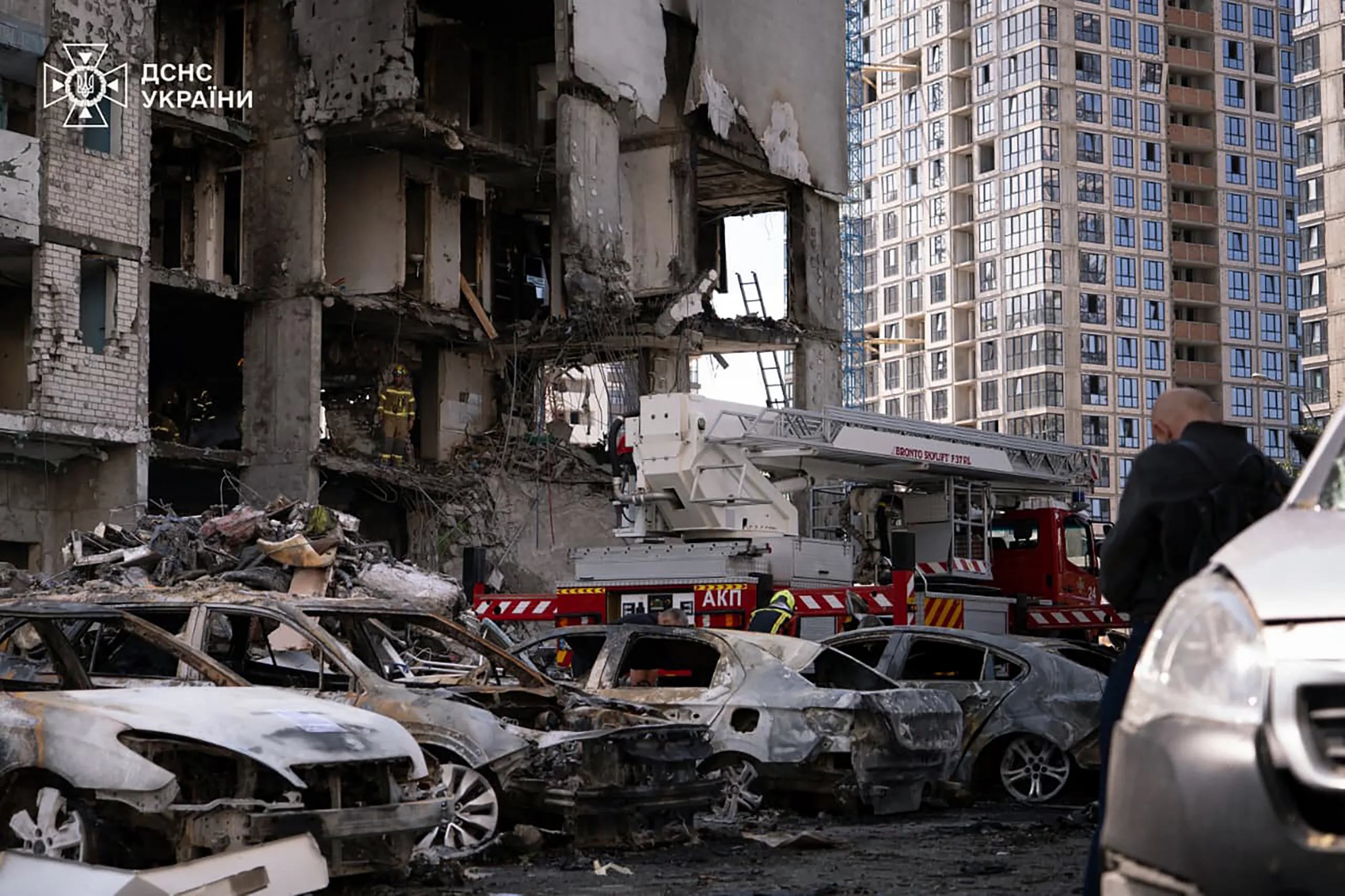 Carros queimados estacionados em frente a um edifício parcialmente destruído por um ataque de mísseis russos à capital ucraniana, Kiev