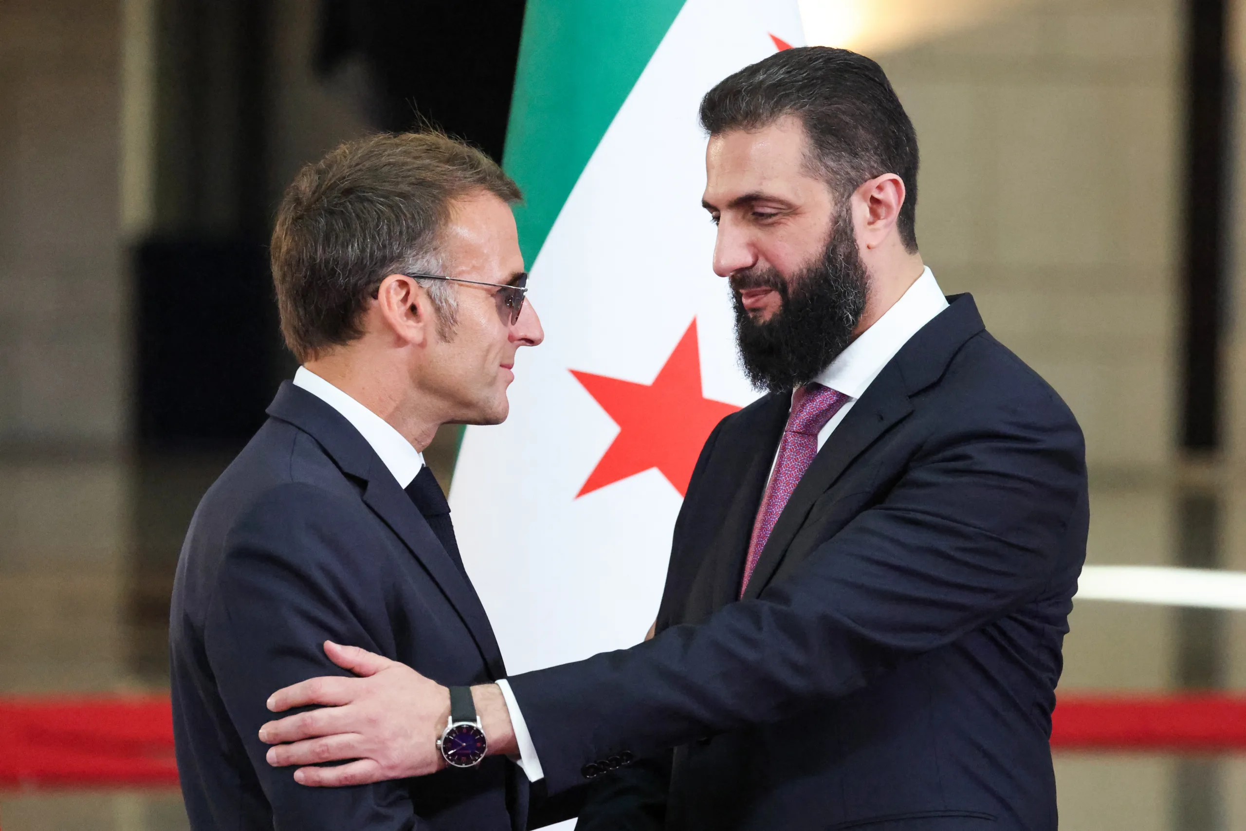 O presidente sírio Ahmed al-Sharaa (à direita) aperta a mão do presidente francês Emmanuel Macron após uma coletiva de imprensa conjunta em Damasco