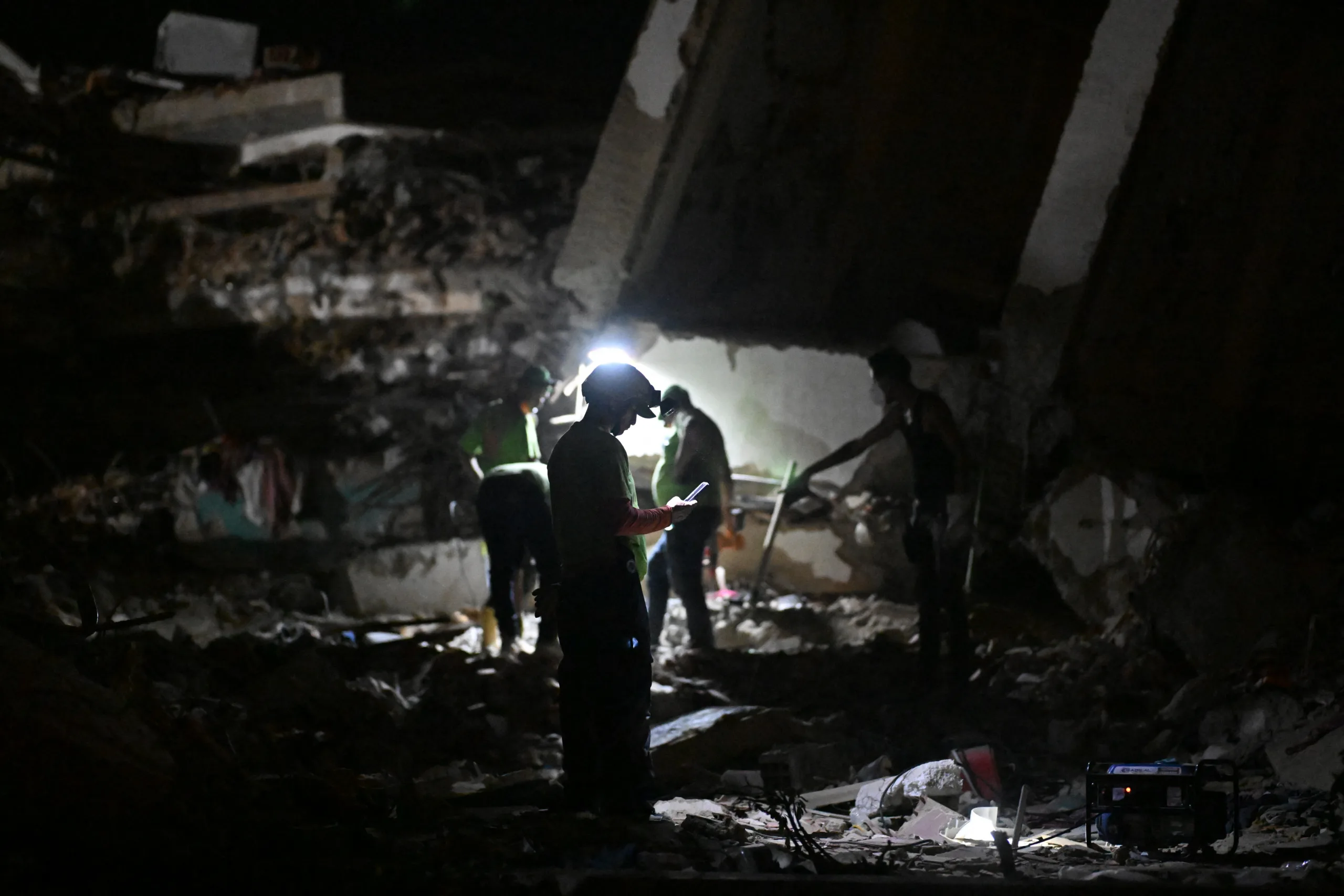 Um socorrista verifica um telefone celular em meio aos escombros de edifícios desabados em Caraballeda, estado de La Guaira, Venezuela, em 7 de julho de 2026, após os terremotos de 24 de junho. Os poderosos terremotos gêmeos que atingiram a Venezuela em 24 de junho deixaram pelo menos 3.685 mortos e quase 17.000 feridos, informou o governo venezuelano em sua mais recente atualização oficial em 7 de julho.