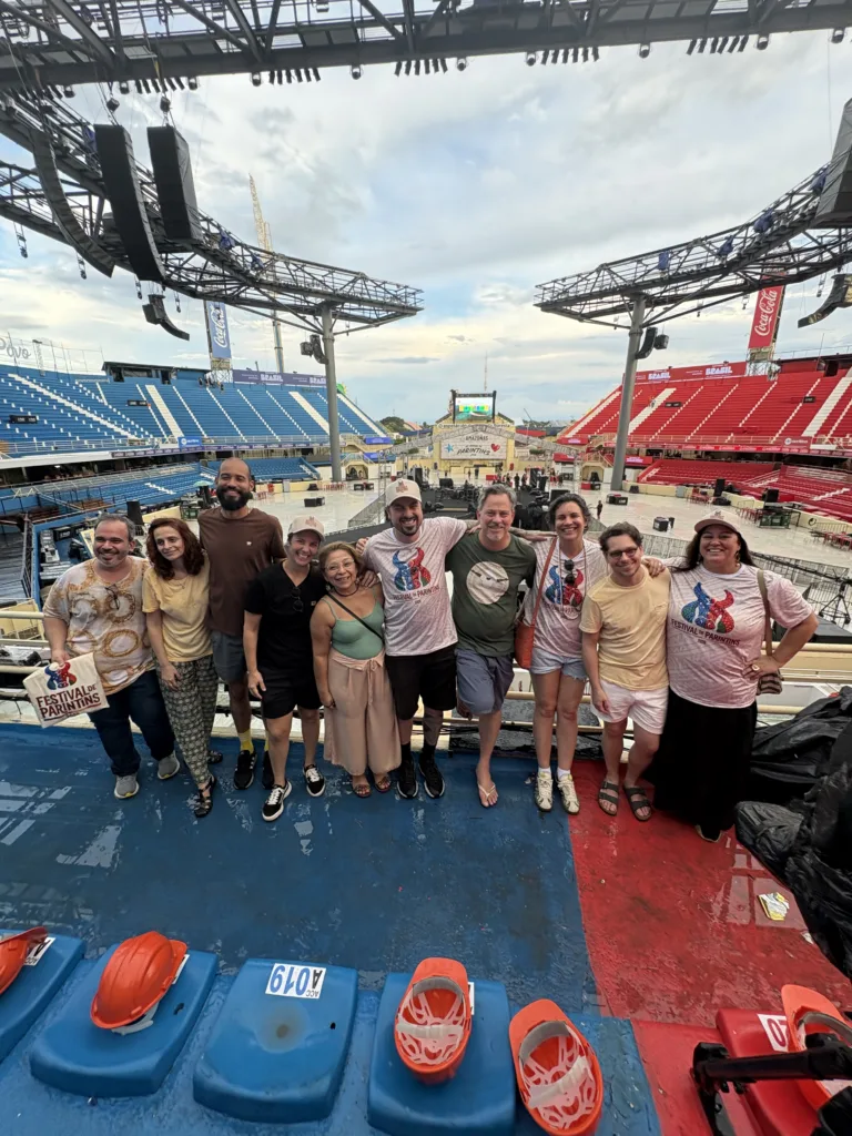 Pessoas dispostas lado à lado no palco do festival com o Bumbódromo de fundo