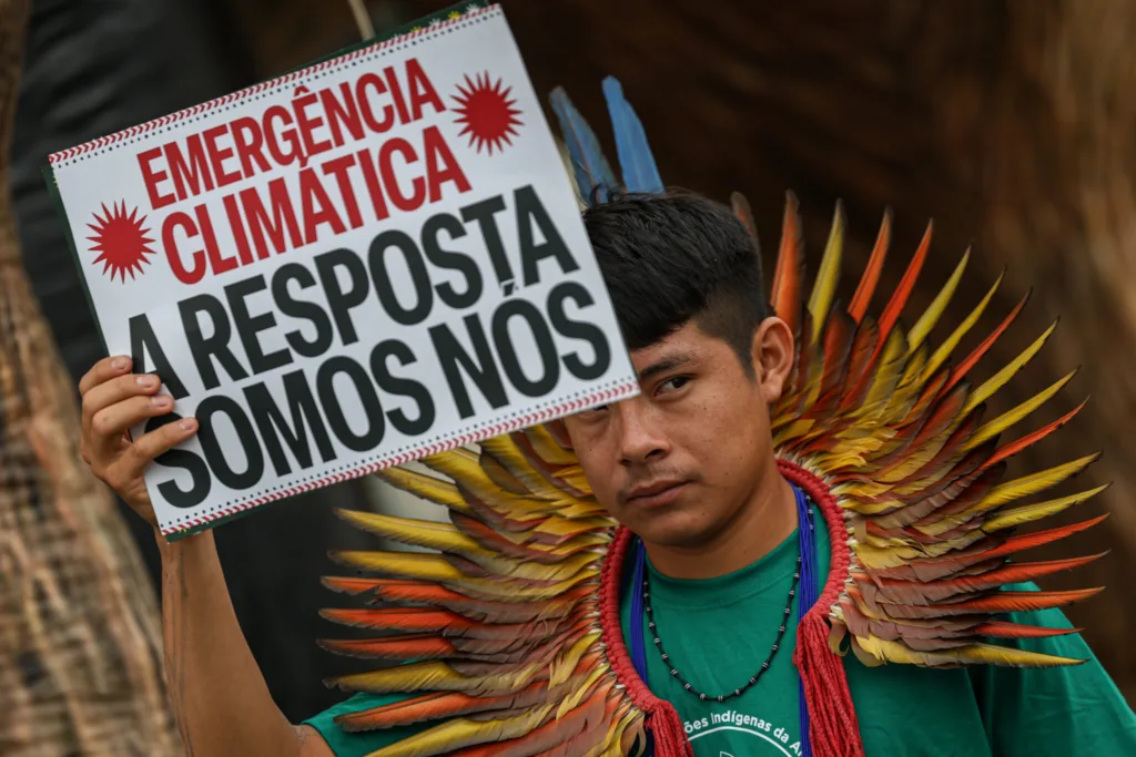 Indígena segura um cartaz com a mensagem "Emergência climática. A resposta somos nós"