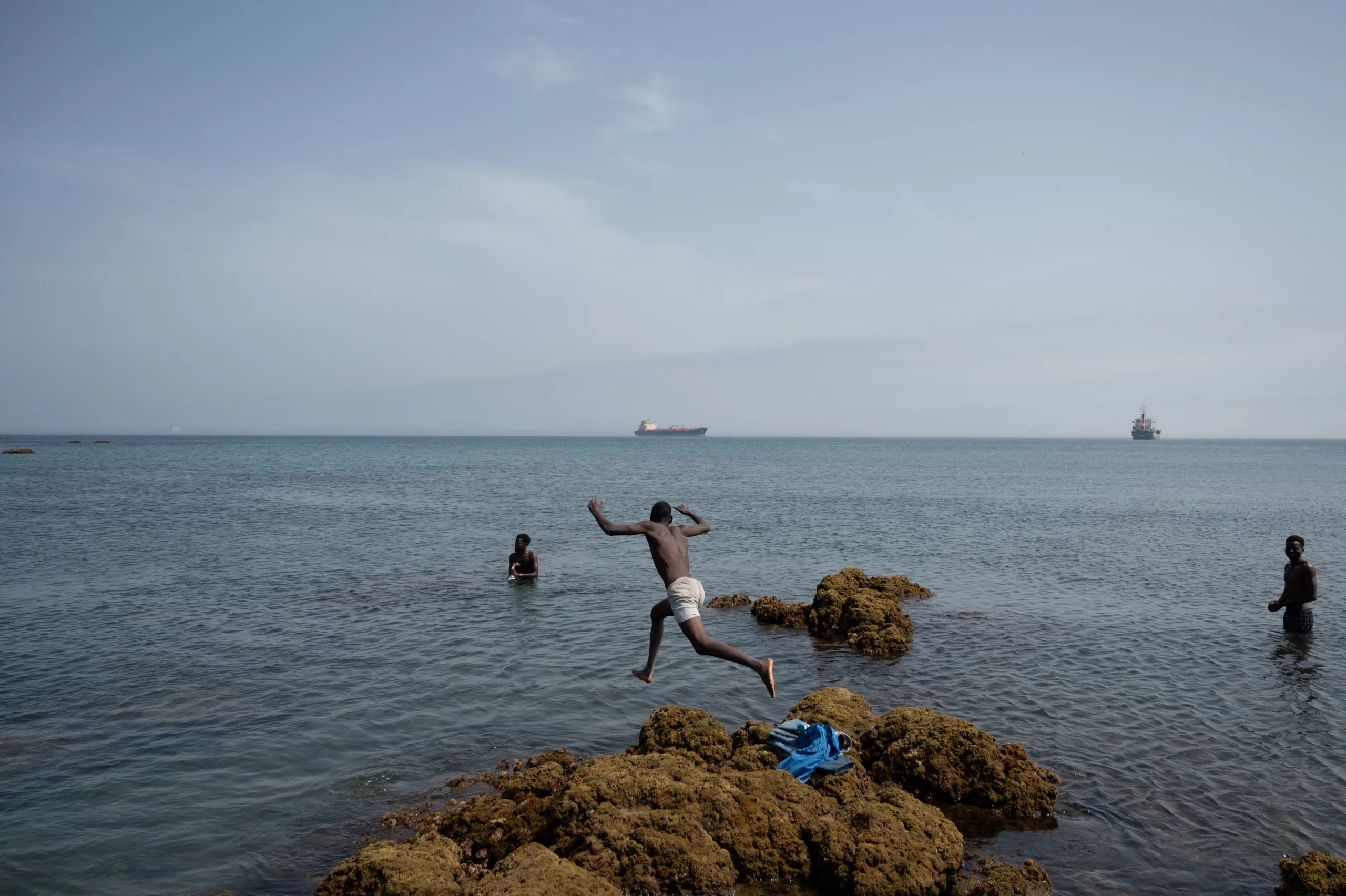 Migrantes no mar da praia de Trampolin enquanto aguardam a entrada no centro de acolhimento