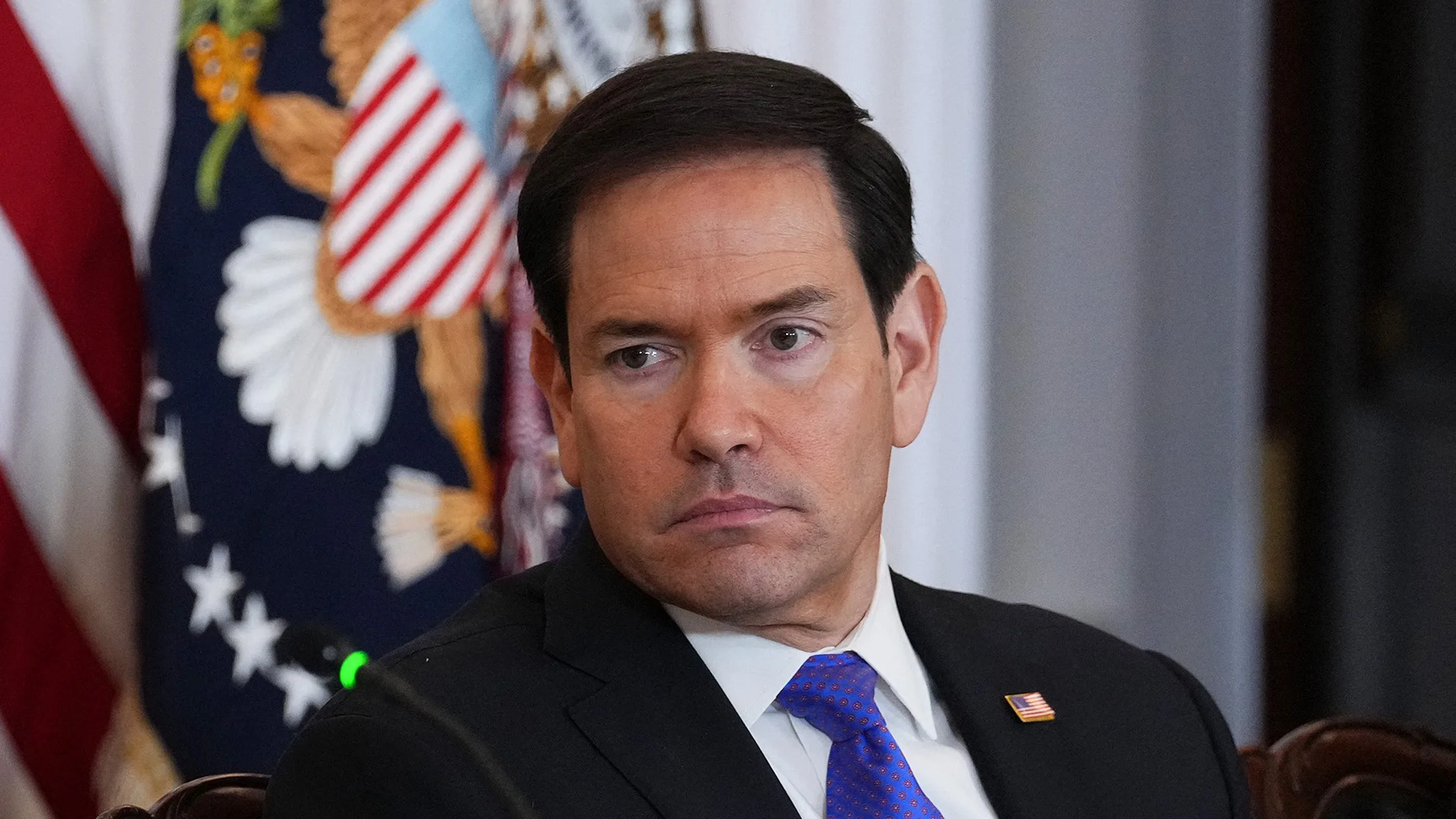 Marco Rubio é um homem de cabelo liso e bronzeado artificial alaranjado, fotografado olhando para o vazio