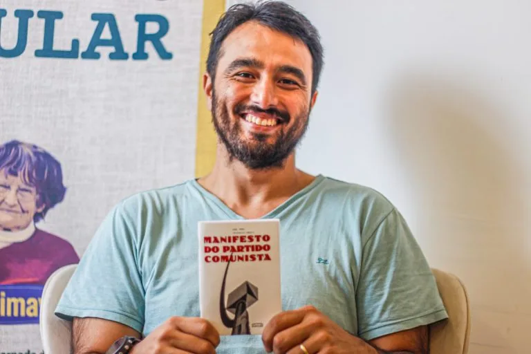 Fotografia de Yoshida. Ele sorri e segura um exemplar do Manifesto Comunista