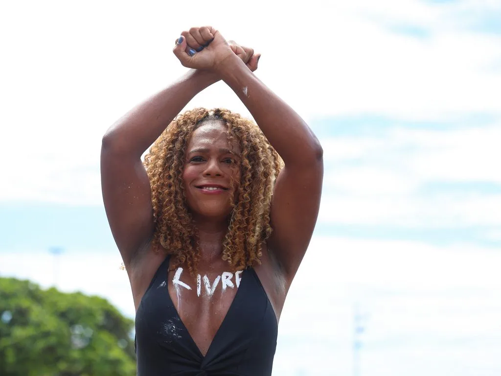Mulher negra posa para foto com os punhos cerrados e usando um body preto e em seu colo se lê "livre"