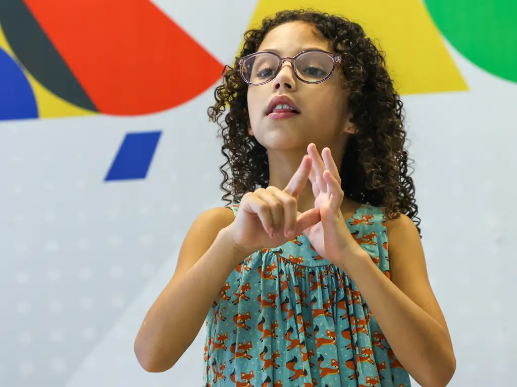 Criança se comunica em língua de sinais durante evento do MEC para comemorar os 22 anos da promulgação Lei 10.436/2002, que reconheceu a Libras como língua oficial