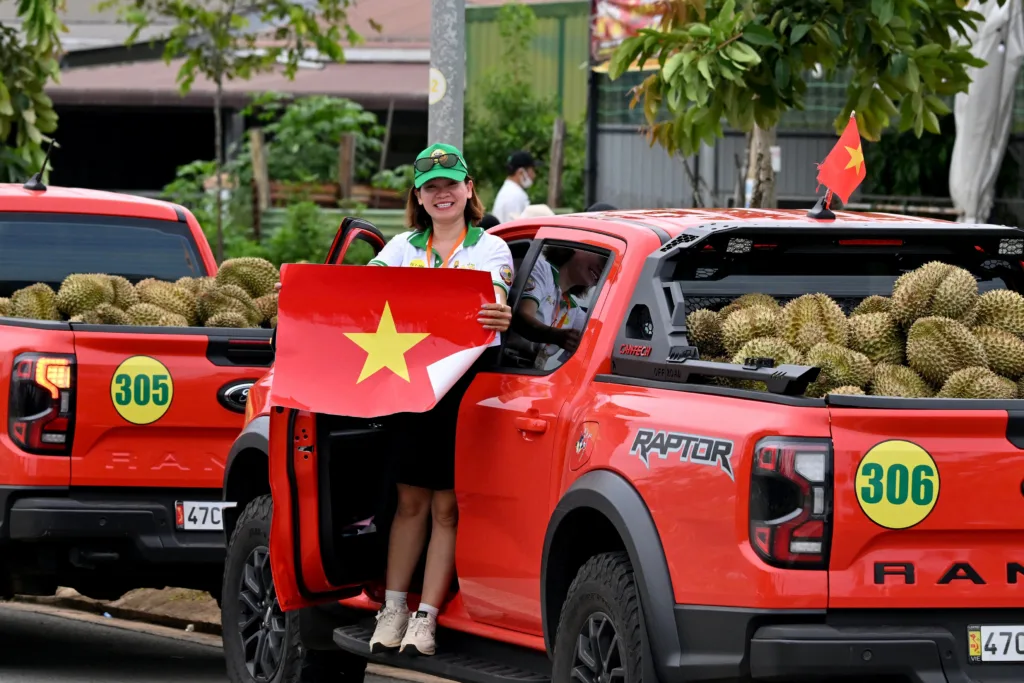Mulher em uma caminhonete carregada de duriões, como parte de um festival dessa fruta, posa com uma bandeira vietnamita na província de Dak Lak, em 16 de agosto de 2026.