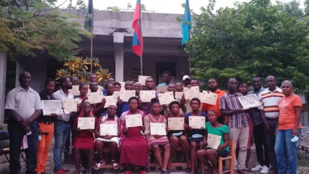 Fotografia mostra uma turma do curso sentada, olhando para a câmera, segurando um certificado em frente ao Centro Nacional de Montrouis