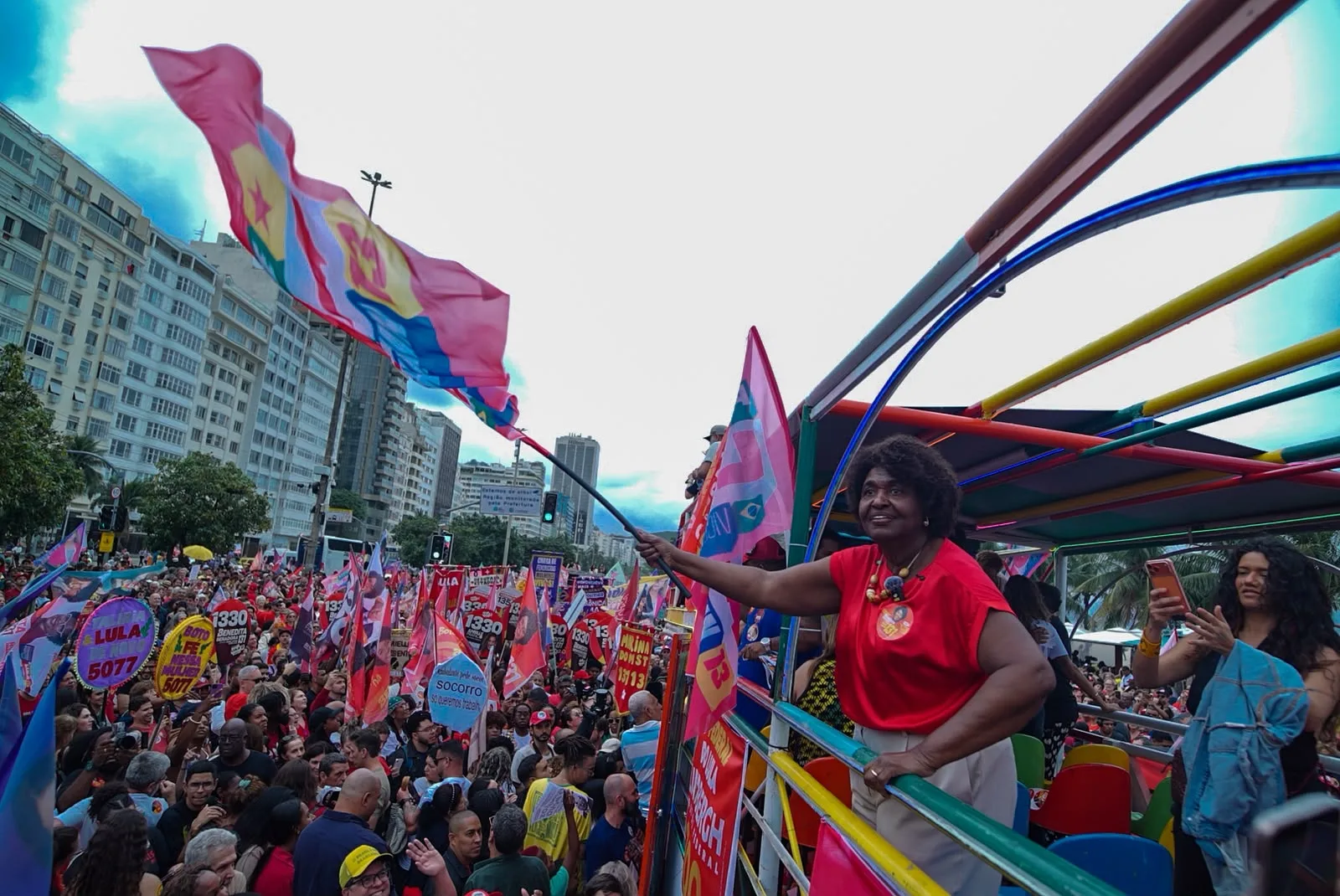 Benedita da Silva balança bandeira do PT no carro de som do comício. No asfalto, milhares de pessoas seguem o carro na orla de Copacabana
