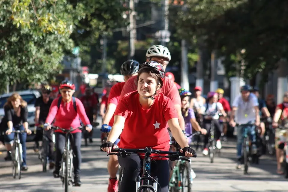 Foto de Luna Zarattini, uma mulher de meia idade, sorrindo e pedalando enquanto usa um capacete, uma camiseta vermelha e uma calça legging.