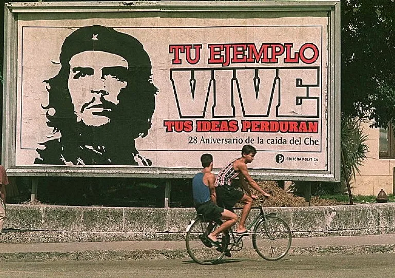Cubanos andam de bicicleta diante de um enorme outdoor com o retrato do lendário revolucionário argentino Ernesto "Che" Guevara, no centro de Havana, Cuba.